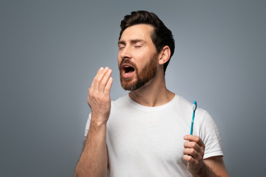 man smelling breath and holding toothbrush