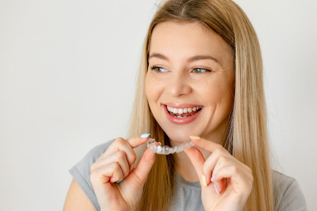 Blonde woman holding clear aligners and smiling